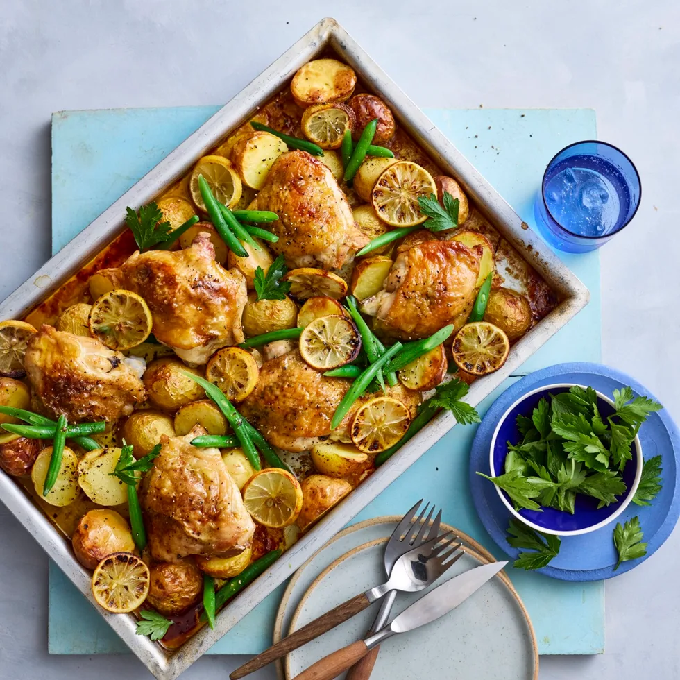 baked lemon chicken and potato tray bake in rectangular tray with knives and forks on the side