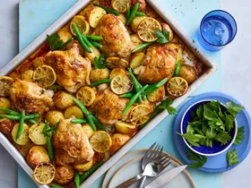 baked lemon chicken and potato tray bake in rectangular tray with knives and forks on the side