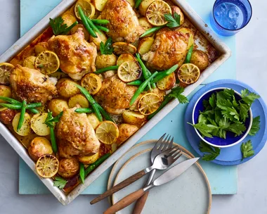baked lemon chicken and potato tray bake in rectangular tray with knives and forks on the side