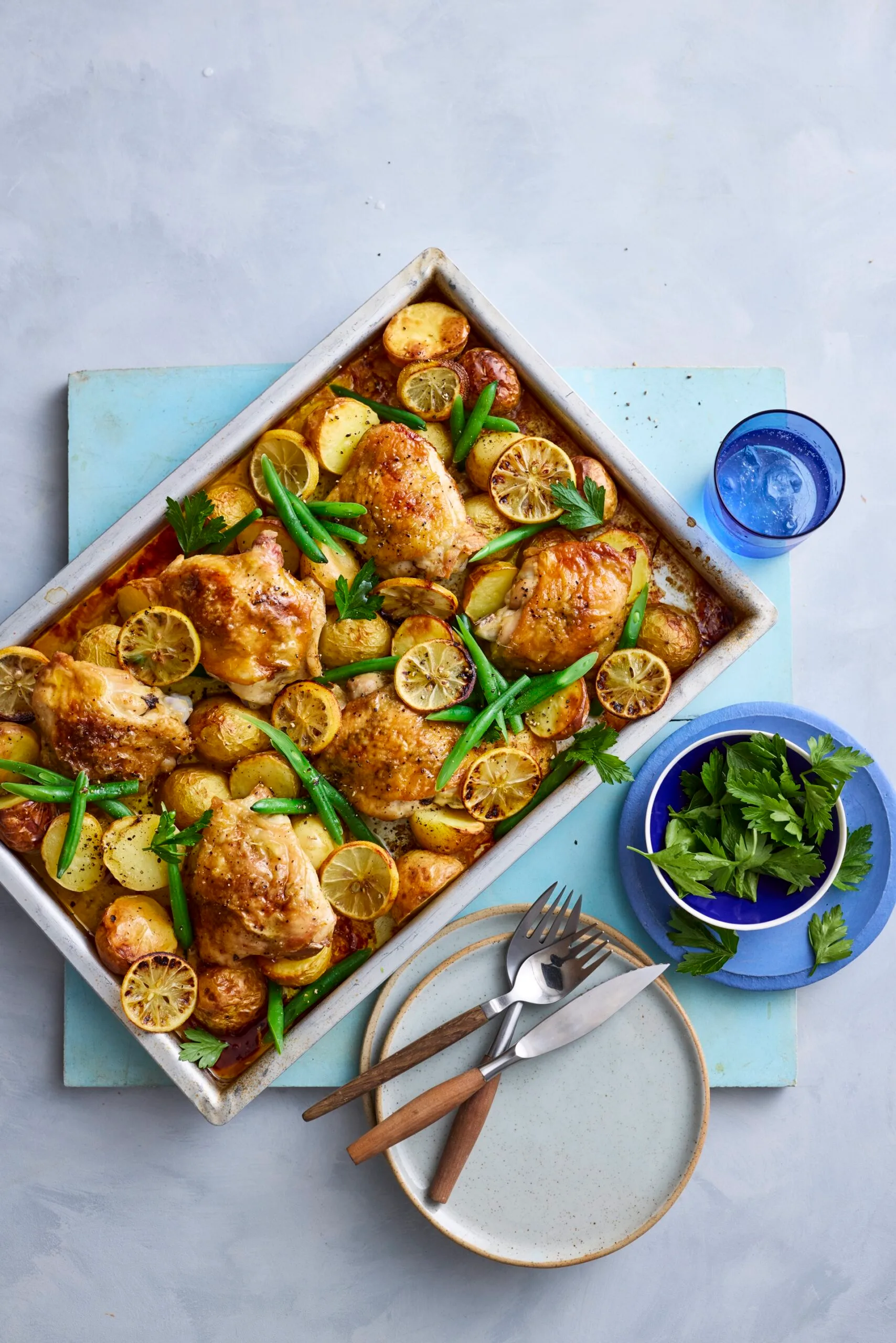 baked lemon chicken and potato tray bake in rectangular tray with knives and forks on the side