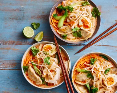 dumpling laksa in three bowls with lime wedges on the side and coriander on top
