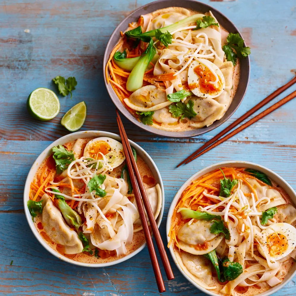 dumpling laksa in three bowls with lime wedges on the side and coriander on top