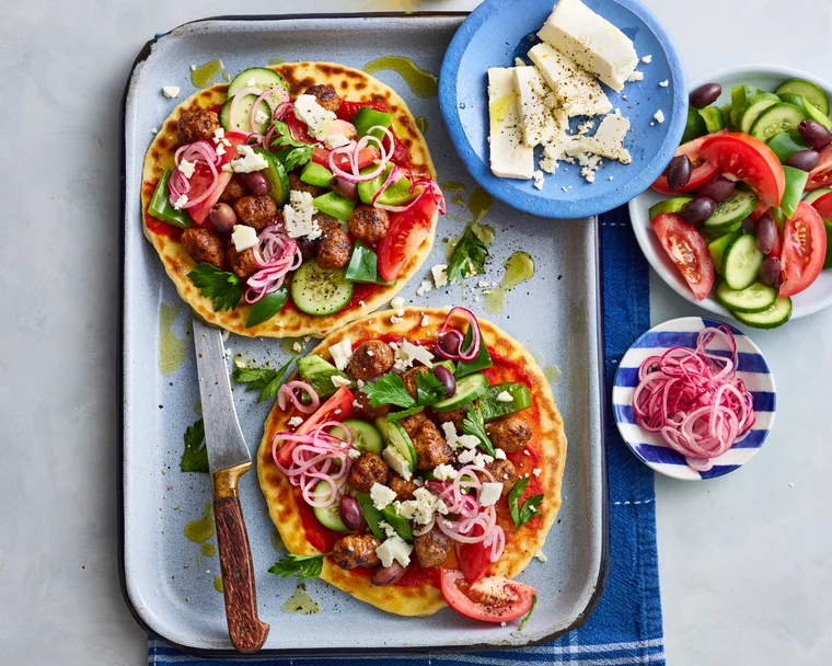 lamb flatbreads with greek salad and pickled onions piled on top on baking tray