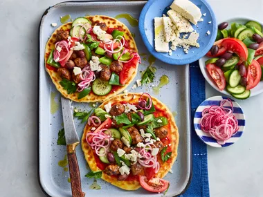 lamb flatbreads with greek salad and pickled onions piled on top on baking tray