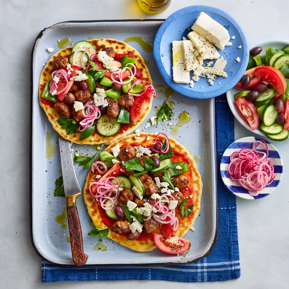 lamb flatbreads with greek salad and pickled onions piled on top on baking tray