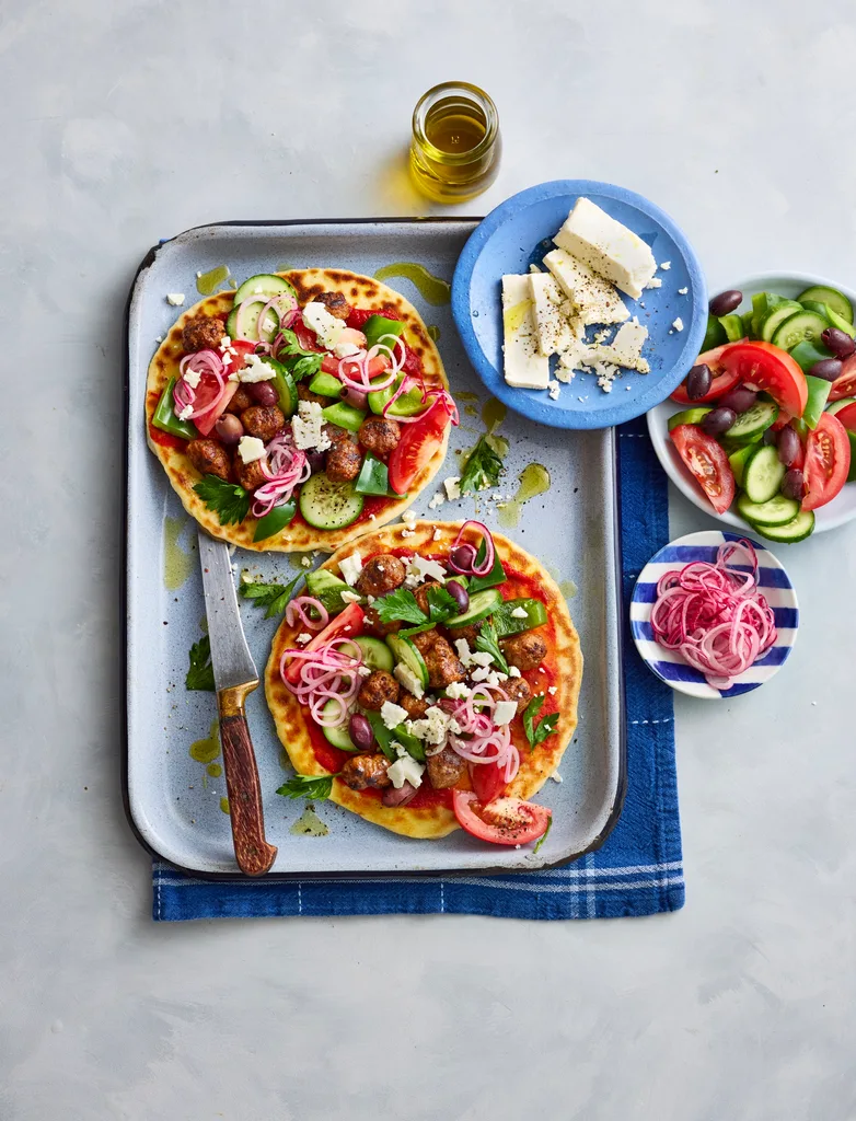 lamb flatbreads with greek salad and pickled onions piled on top on baking tray