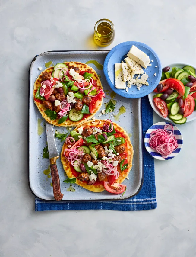 lamb flatbreads with greek salad and pickled onions piled on top on baking tray