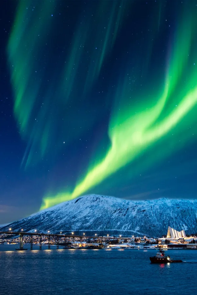 northern lights in green and blue on night sky over city of tromso in norway