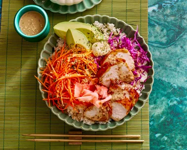 teriyaki chicken bowl with sushi rice shredded carrot pickled ginger and sesame dressing in small bowl on the side