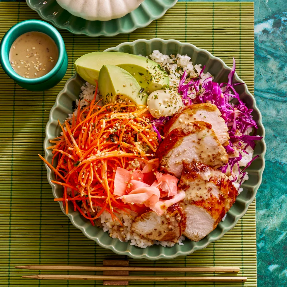 teriyaki chicken bowl with sushi rice shredded carrot pickled ginger and sesame dressing in small bowl on the side