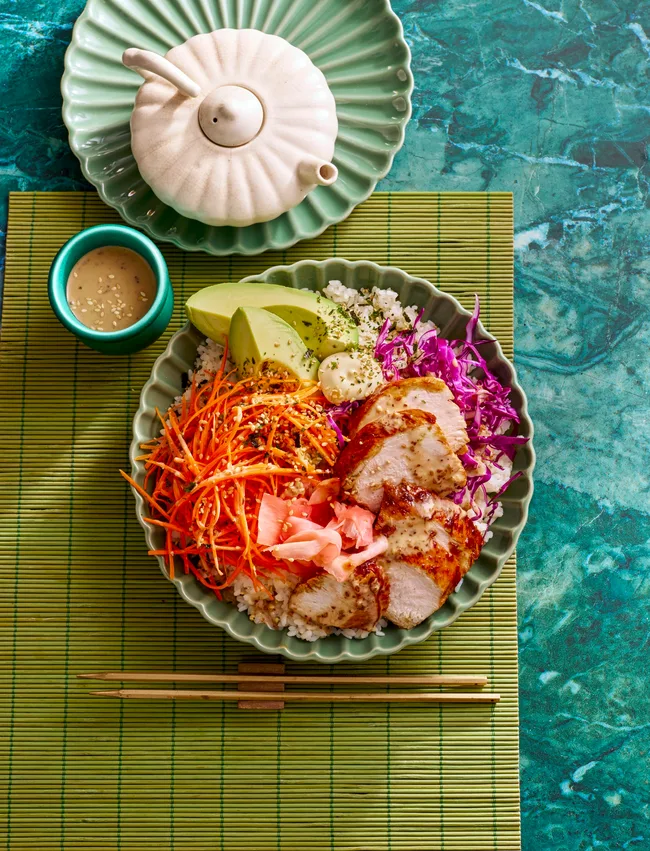 teriyaki chicken bowl with sushi rice shredded carrot pickled ginger and sesame dressing in small bowl on the side