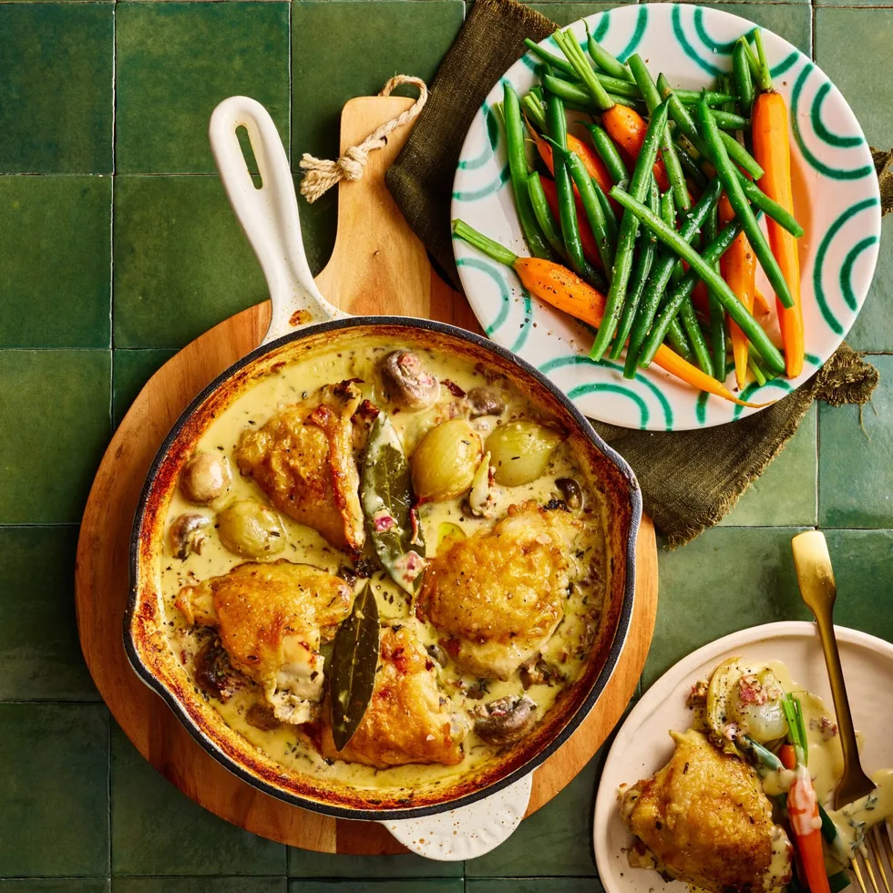 chicken fricassee in cooking pan with chicken on top and sauce on bottom with fresh carrots and beans on the side