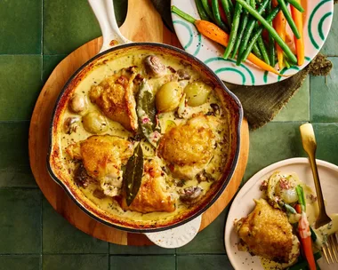 chicken fricassee in cooking pan with chicken on top and sauce on bottom with fresh carrots and beans on the side