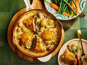 chicken fricassee in cooking pan with chicken on top and sauce on bottom with fresh carrots and beans on the side