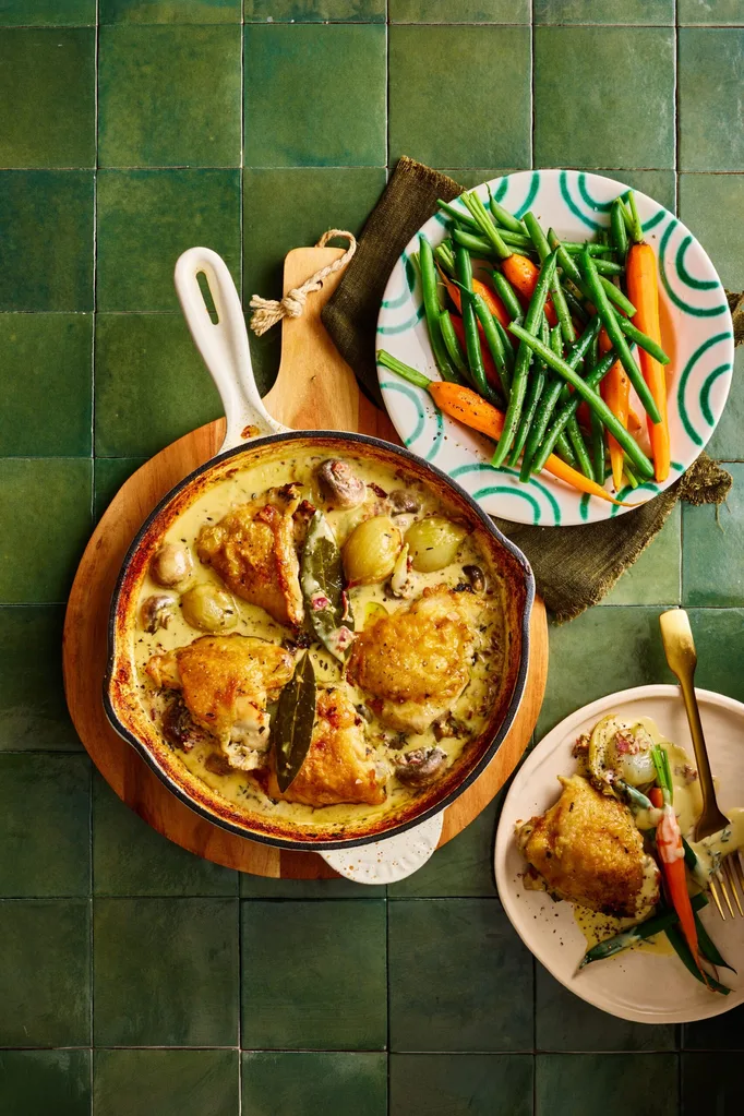 chicken fricassee in cooking pan with chicken on top and sauce on bottom with fresh carrots and beans on the side