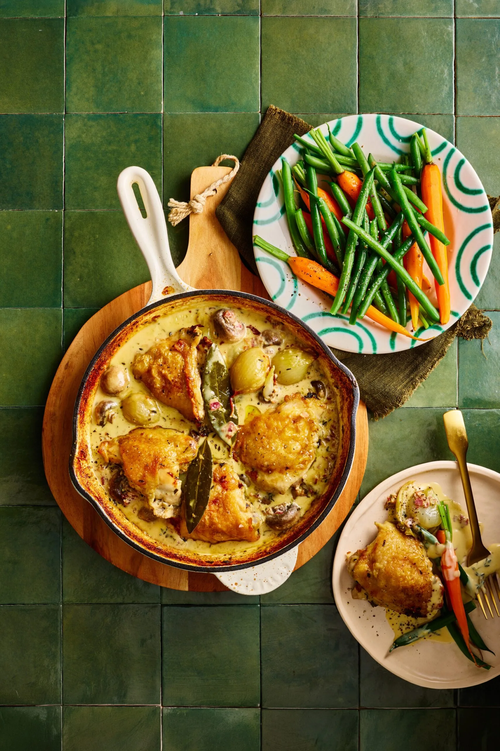 chicken fricassee in cooking pan with chicken on top and sauce on bottom with fresh carrots and beans on the side