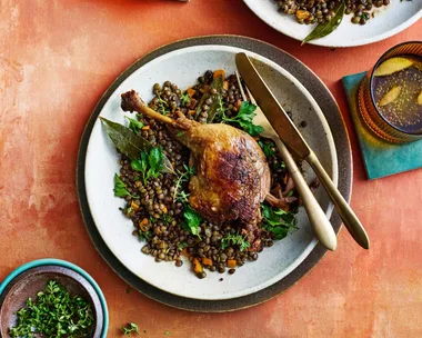duck confit leg on top of french style lentils with white bowl underneath