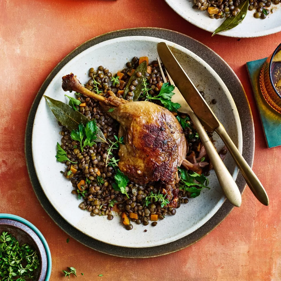 duck confit leg on top of french style lentils with white bowl underneath