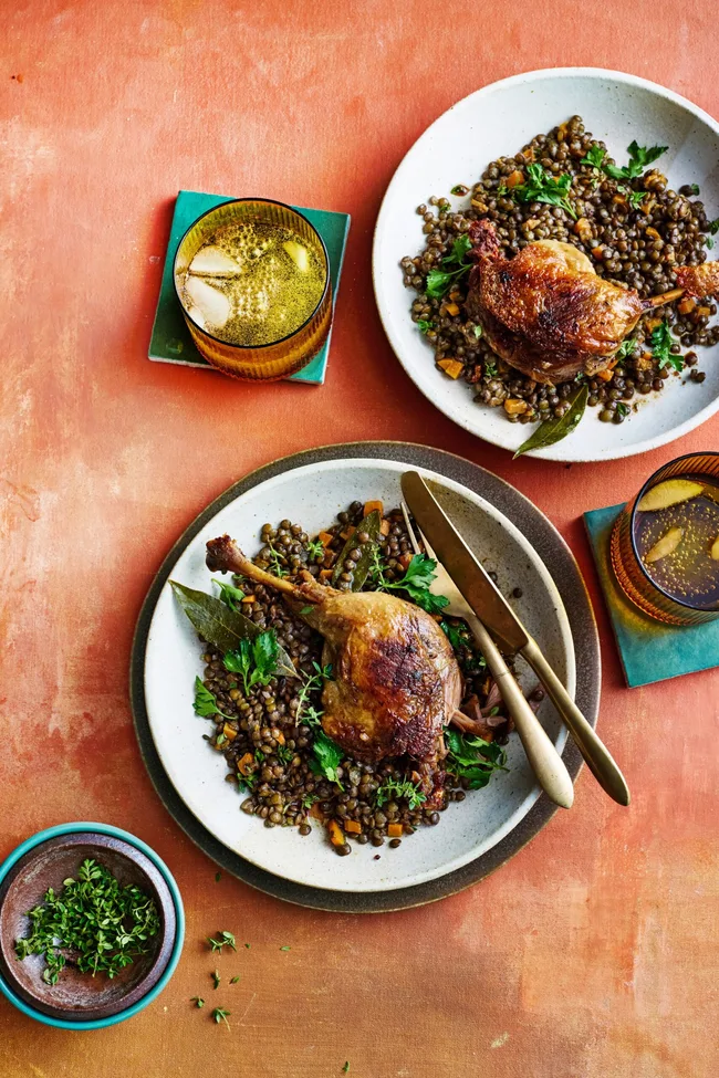 duck confit leg on top of french style lentils with white bowl underneath