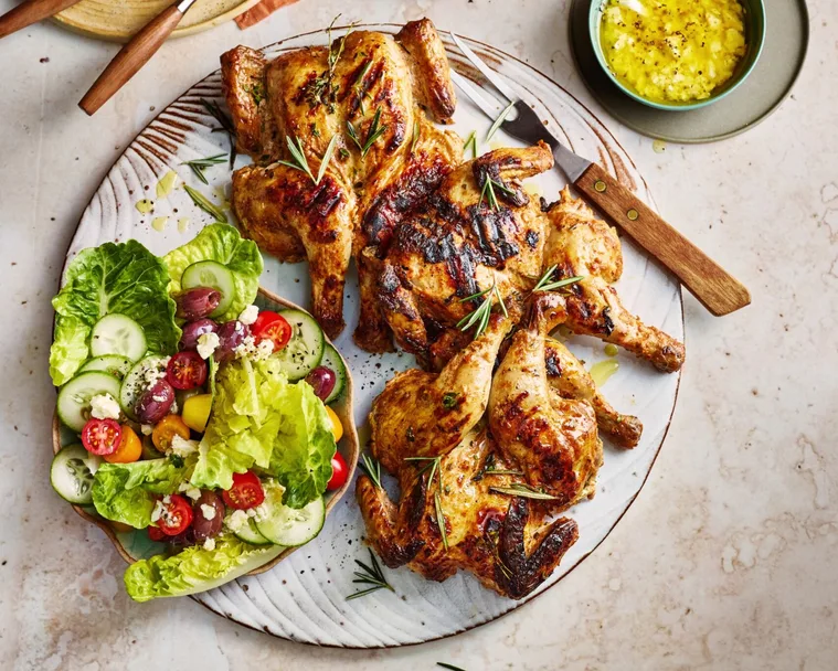 poussin with greek salad small chickens on plate with salad and dressing on the side