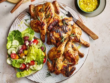 poussin with greek salad small chickens on plate with salad and dressing on the side