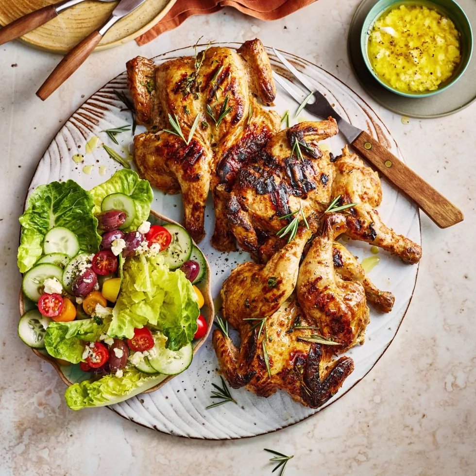 poussin with greek salad small chickens on plate with salad and dressing on the side