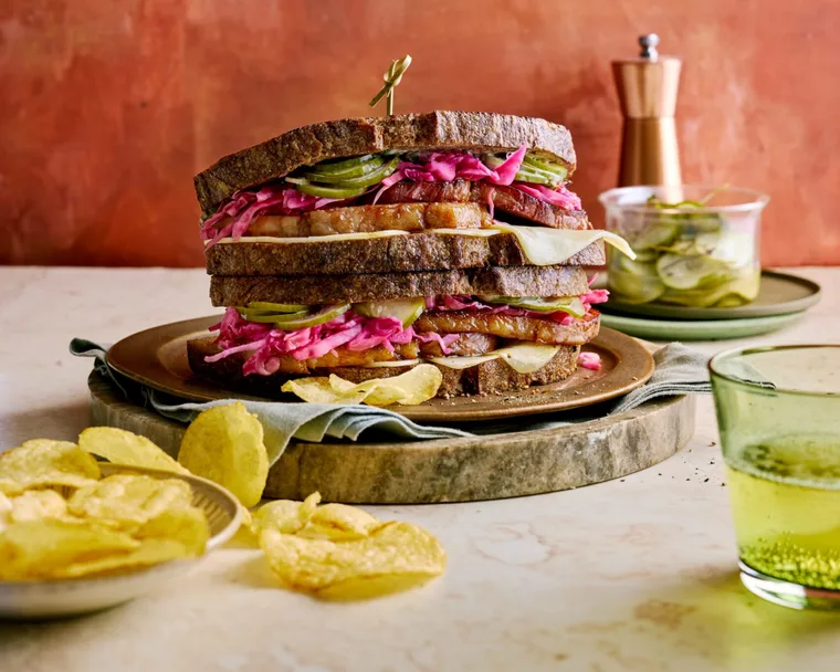 reuben sandwich with homemade pastrami and pickles with chips next to it