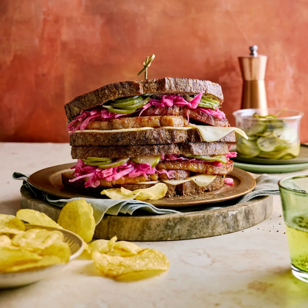 reuben sandwich with homemade pastrami and pickles with chips next to it