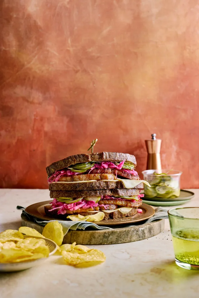 reuben sandwich with homemade pastrami and pickles with chips next to it