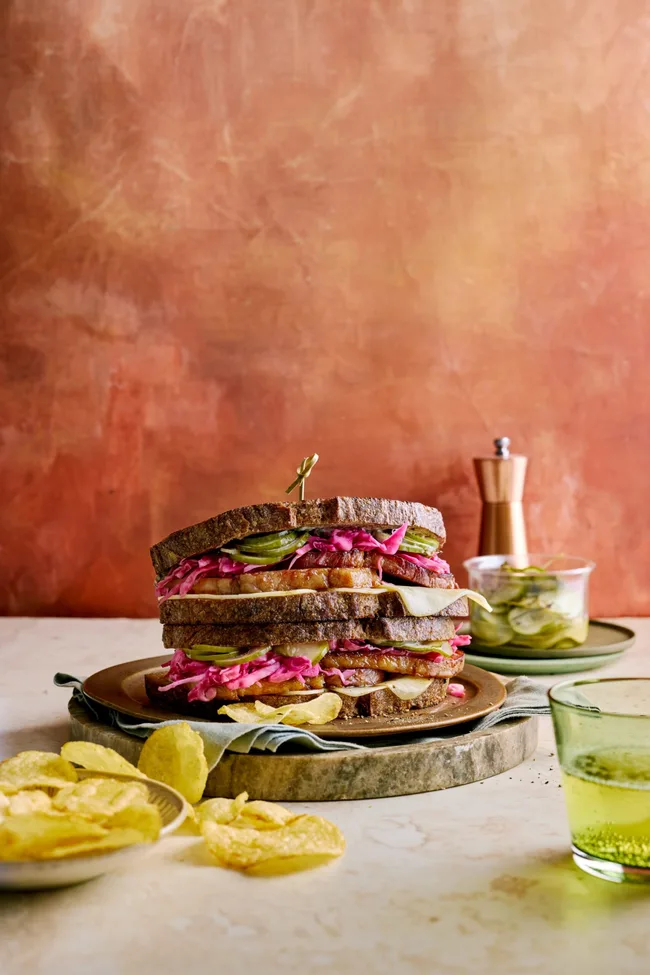 reuben sandwich with homemade pastrami and pickles with chips next to it