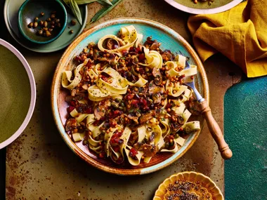 mushroom sage and pancetta pasta in bowl with tagliatelle pasta and chopping board underneath