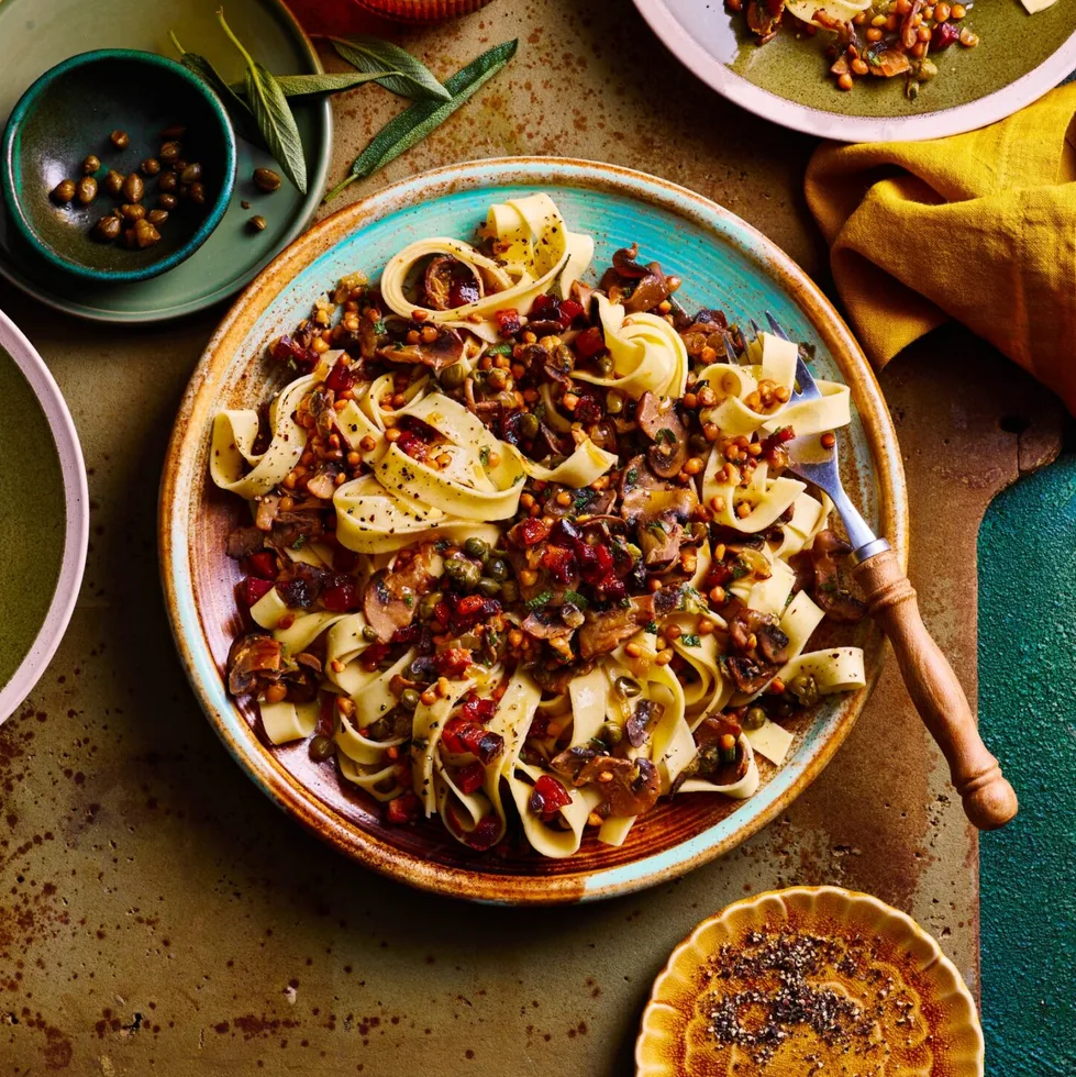 mushroom sage and pancetta pasta in bowl with tagliatelle pasta and chopping board underneath
