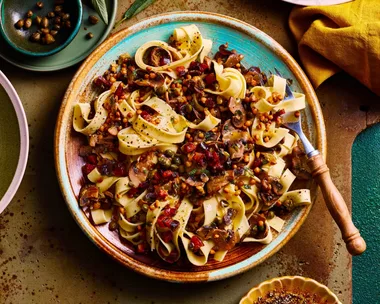 mushroom sage and pancetta pasta in bowl with tagliatelle pasta and chopping board underneath