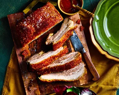 pork belly rotisserie recipe with huge slices cute into it and barbecue sauce on the side