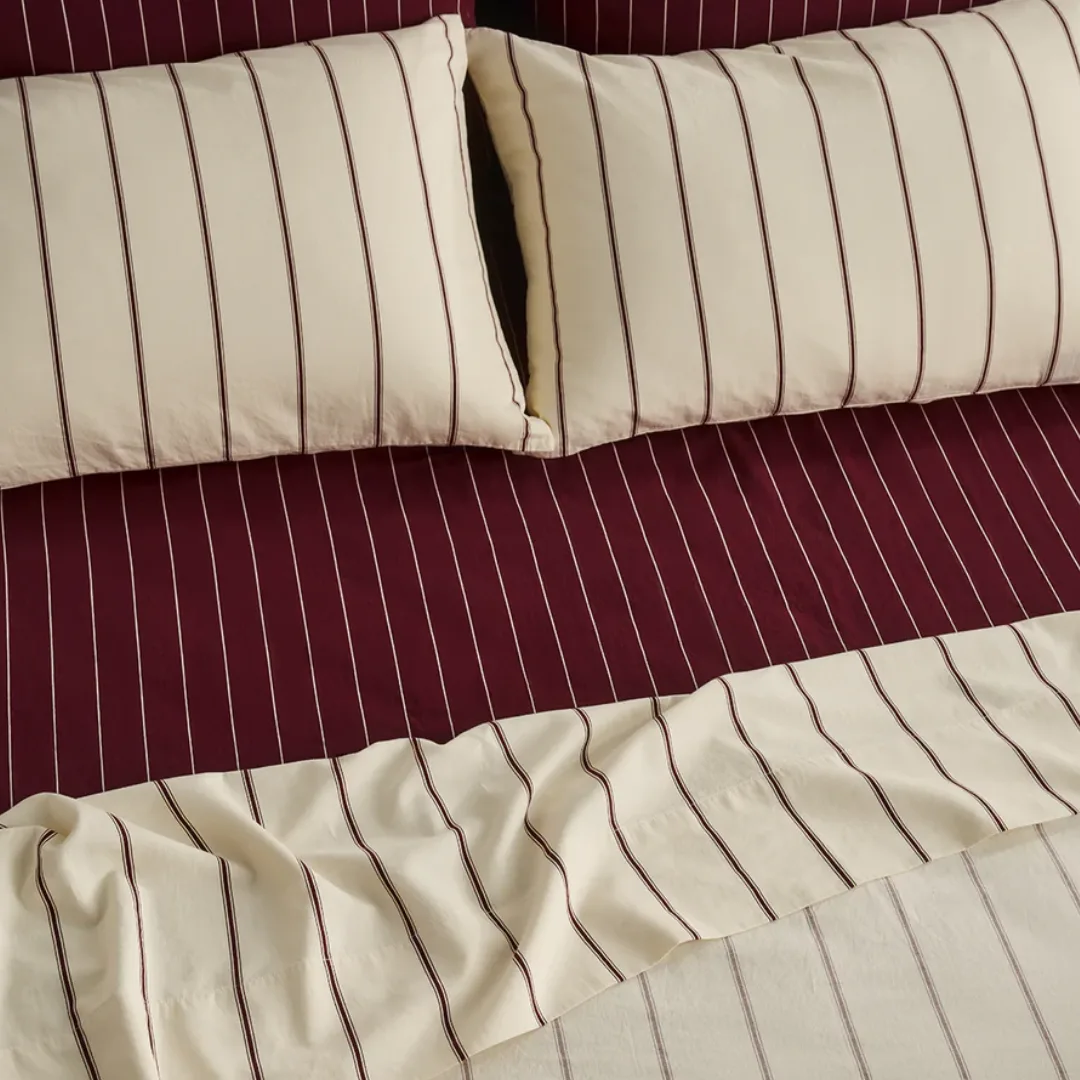 a close up of a bed dressed in wine toned and warm cream striped bedding from Hommey
