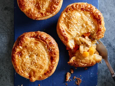 apricot chicken pies on blue tray with one crumbled showing the inside