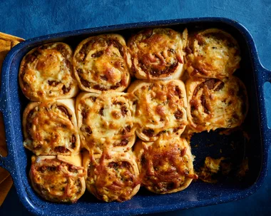 sausage sizzle scrolls in baking tray with one missing on blue table