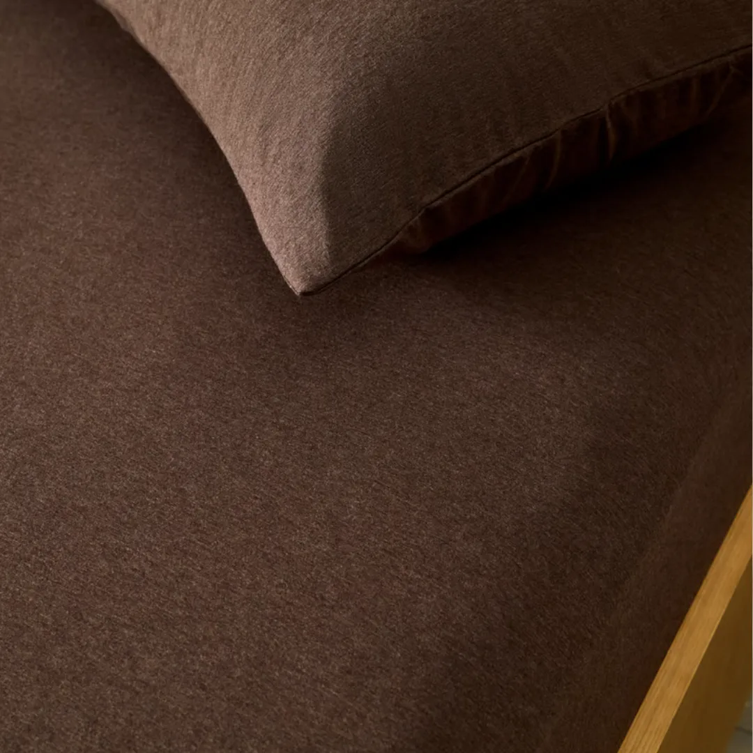 Close up image of a bed with a chocolate brown jersey fitted sheet, and matching pillowcase from Adairs