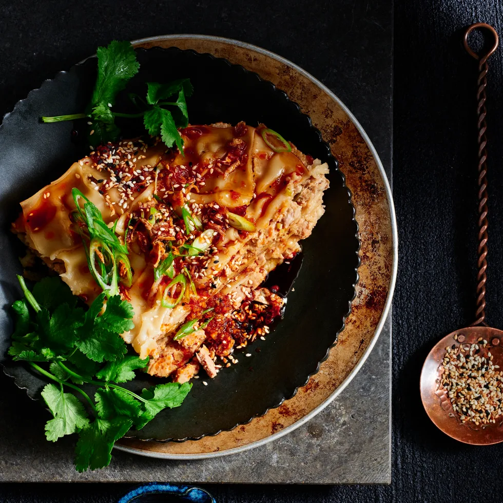 Slow cooker lazy dumpling lasagne with chilli sauce and sesame seeds next to it to garnish