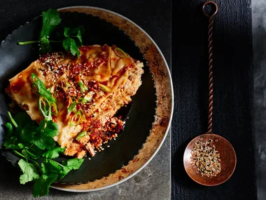 Slow cooker lazy dumpling lasagne with chilli sauce and sesame seeds next to it to garnish