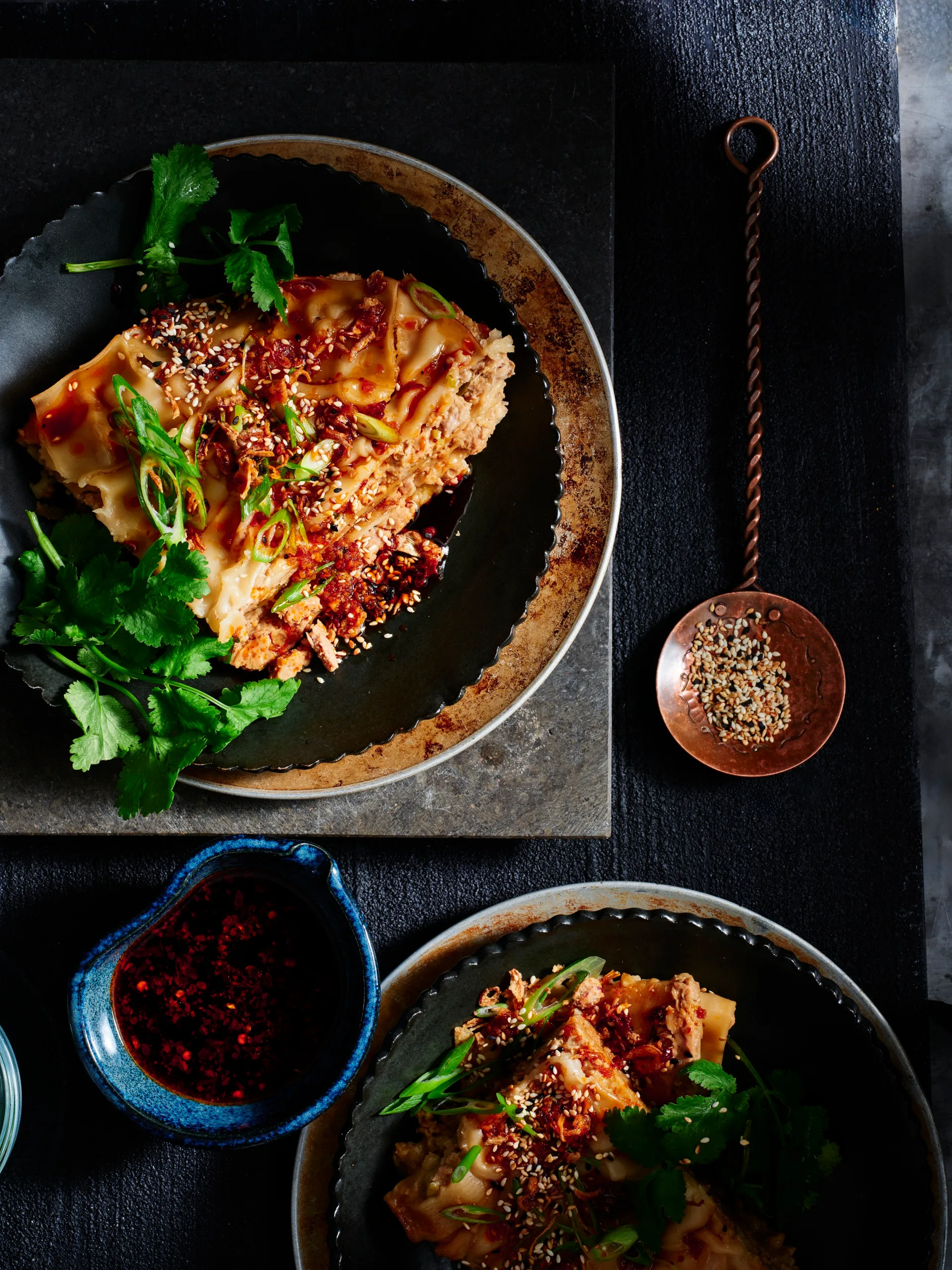 Slow cooker lazy dumpling lasagne with chilli sauce and sesame seeds next to it to garnish