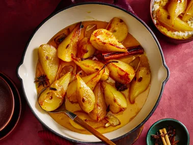 Spiced ginger pears in an enamelled cast-iron frying pan with a wooden spoon