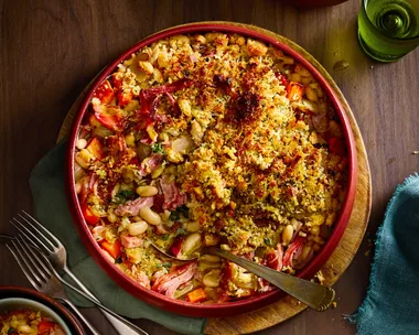 ham hock and white bean bake with breadcrumbs toasted on top in red bowl with spoon sticking out