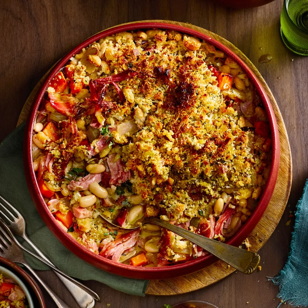 ham hock and white bean bake with breadcrumbs toasted on top in red bowl with spoon sticking out