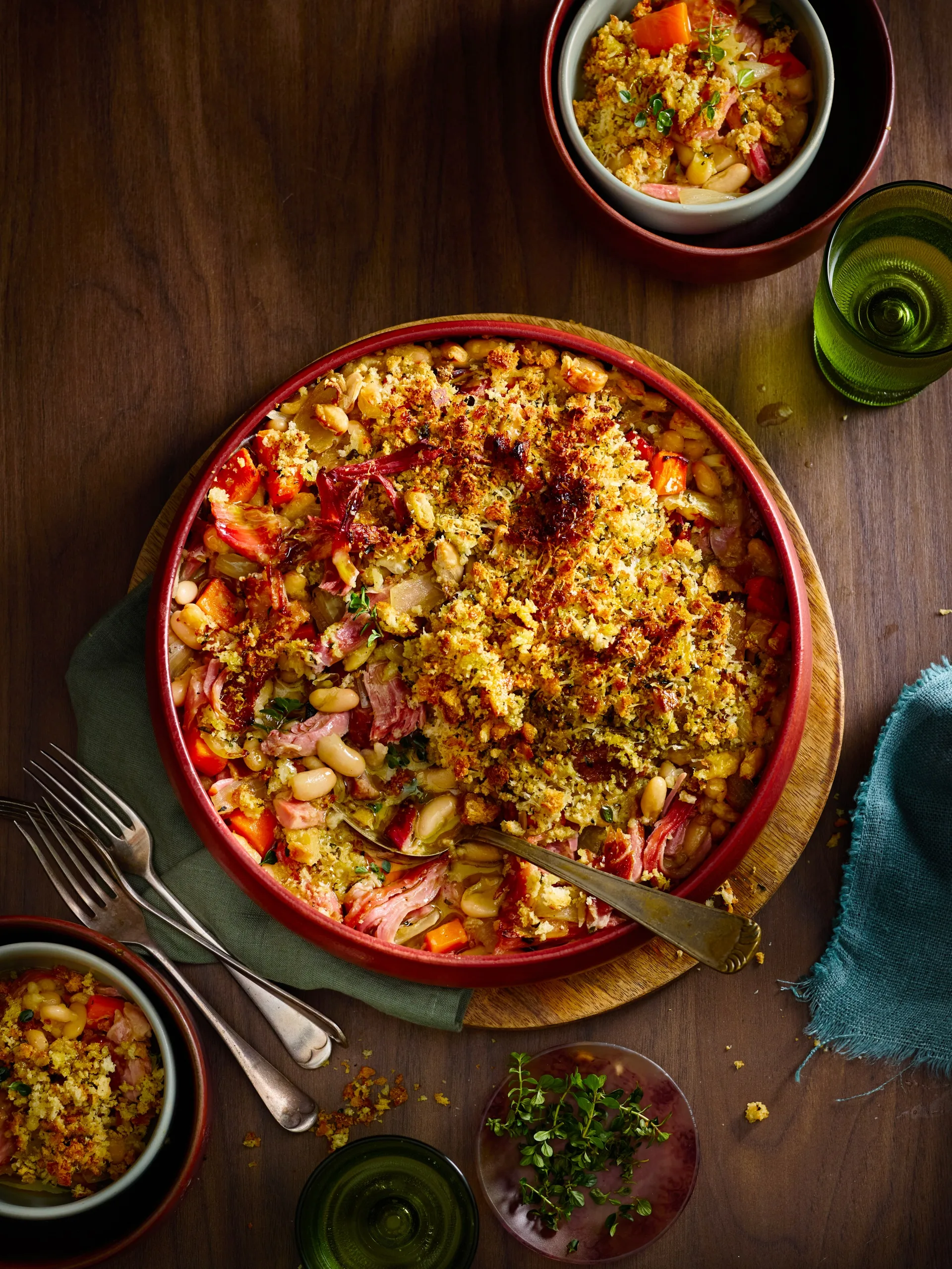 ham hock and white bean bake with breadcrumbs toasted on top in red bowl with spoon sticking out