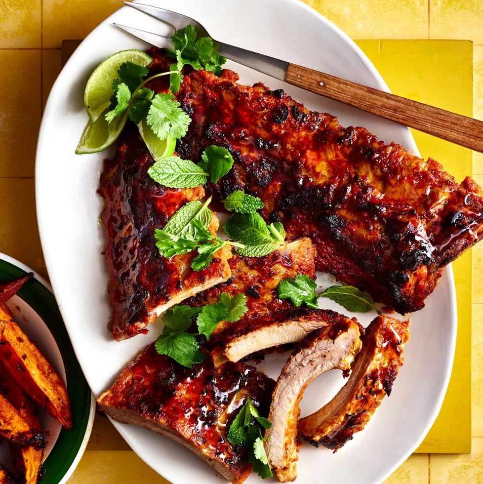 satay pork ribs on white bowl with herbs on top and cheeks of lime on the side