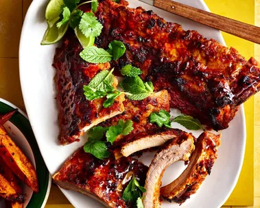 satay pork ribs on white bowl with herbs on top and cheeks of lime on the side