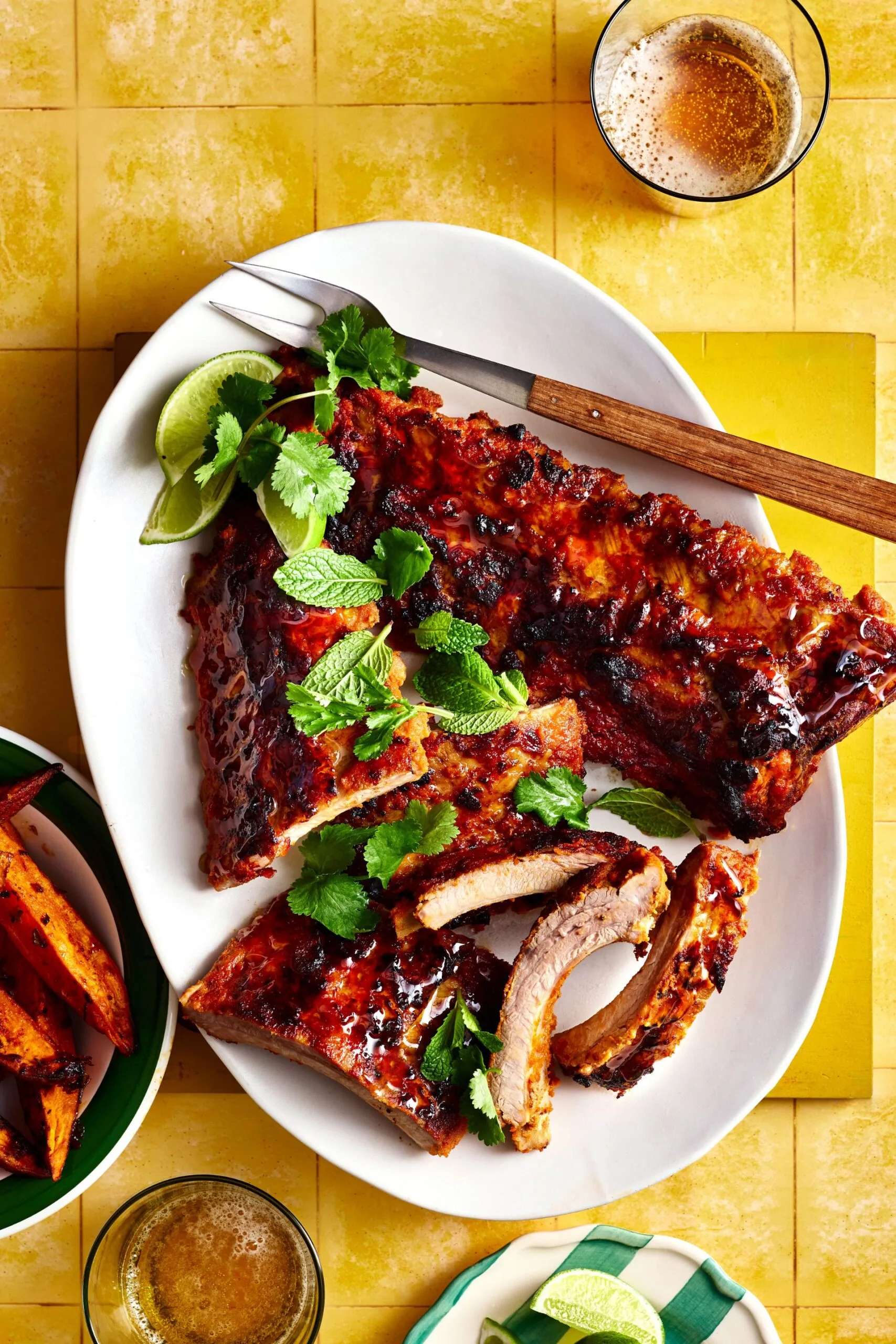 satay pork ribs on white bowl with herbs on top and cheeks of lime on the side