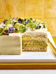 swedish sandwich cake with edible flowers and ribbons on cucumber on top of cream cheese 'icing'. layers inside include rye bread, smoked salmon, egg salad and cucumber