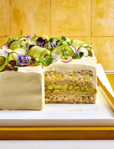 swedish sandwich cake with edible flowers and ribbons on cucumber on top of cream cheese 'icing'. layers inside include rye bread, smoked salmon, egg salad and cucumber